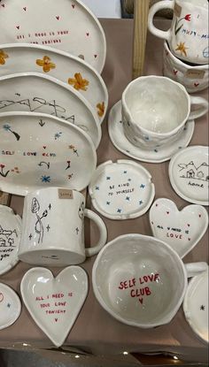 a table topped with lots of white dishes and bowls covered in handwritten words on them