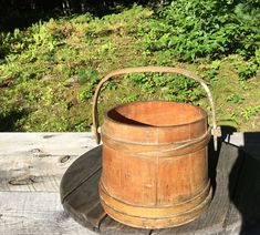 an old wooden bucket sitting on top of a wooden table next to some grass and bushes