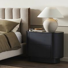 a white vase sitting on top of a nightstand next to a bed