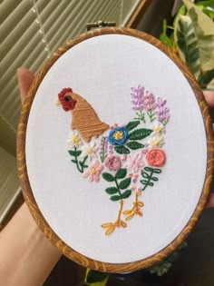 a person holding up a wooden hoop with flowers and a chicken on it in front of a window