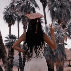 a woman wearing a graduation cap and gown standing in front of palm trees with her hands up