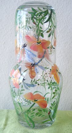 a glass vase with flowers painted on the side and green stems in the bottom, sitting on a table