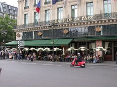 people are walking and sitting on the sidewalk in front of a restaurant