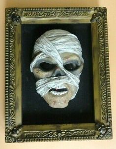 an old mask hanging on the wall in a gold frame with white paper wrapped around it