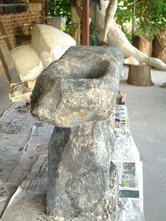 a large stone statue sitting on top of a newspaper paper covered table next to a tree