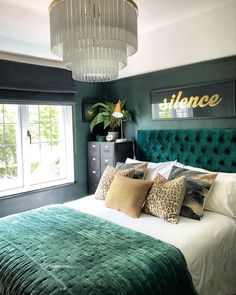 a bedroom with green velvet headboard and white bedding, chandelier above the bed