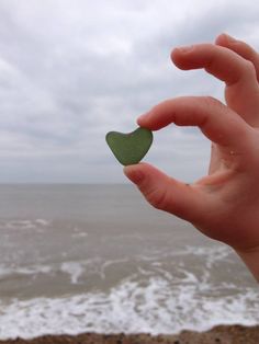 a hand holding a piece of green sea glass in front of the ocean with waves