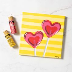 two heart shaped lollipops on a yellow and white striped background next to some glue