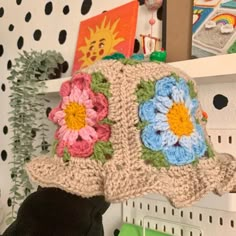 a crocheted hat with flowers on it sitting on a shelf in a room