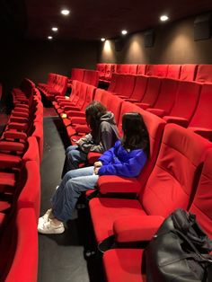 two people sitting on red seats in an empty theater