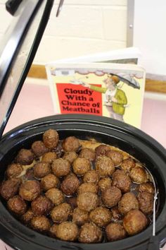 a black crock pot filled with meatballs next to a book on a table