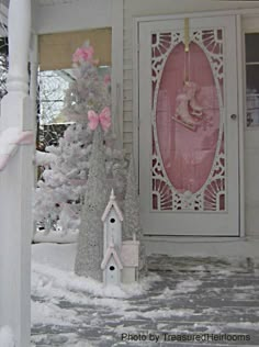 a white house with a pink door and christmas trees in the front yard covered in snow