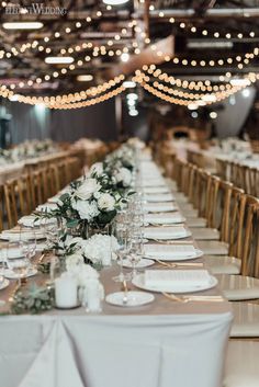 a long table with white flowers and greenery is set for an elegant wedding reception