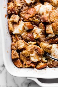 a white casserole dish filled with bread and stuffing, topped with a spoon