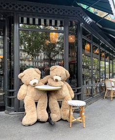 two large teddy bears sitting at a table in front of a restaurant with chairs and tables