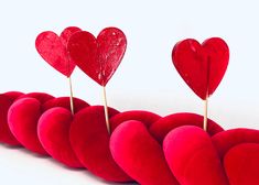 red heart shaped cushions lined up in the shape of a long line with pins sticking out of them