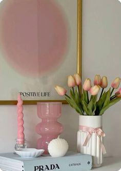 pink tulips are in a vase on top of a book and some seashells