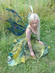 a woman dressed as a fairy sitting in the grass with her hands on her knees