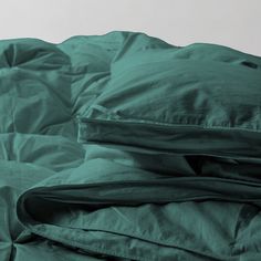 an unmade bed with green sheets and pillows