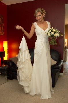 a woman in a white wedding dress holding a bouquet and pointing at something on the wall