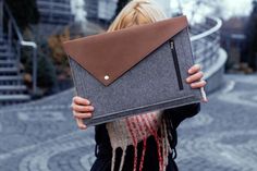 a woman is holding up a gray and brown bag with an envelope on her shoulder