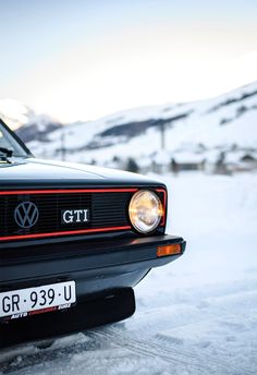 the front end of a black volkswagen gti parked on snow covered ground with mountains in the background