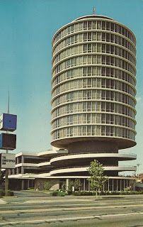 an old photo of a large building in the middle of a street with cars driving by