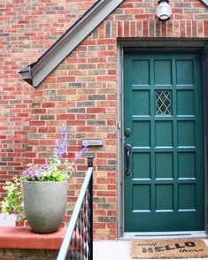 a green front door on a brick house with potted plants and flowers in the foreground