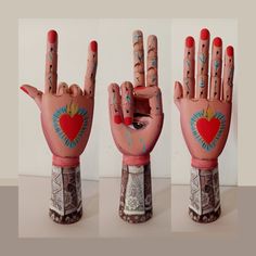 three images of hands with painted designs on them, one holding a heart and the other showing two fingers