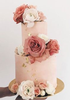 a hand holding a pink and white cake with flowers on the top, in front of a white background