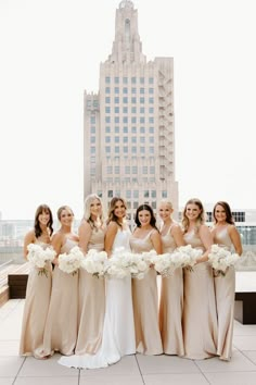 a group of women standing next to each other in front of a tall building with white flowers