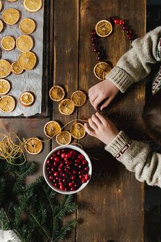 two people are making orange slices and cranberries on a wooden table with christmas decorations