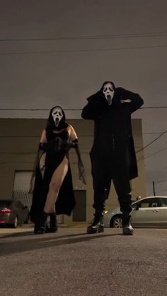 two people wearing masks and standing in the middle of an empty parking lot at night