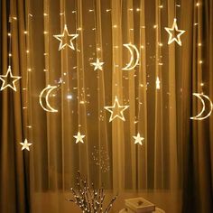 stars and moon string lights are hanging from the ceiling above a window with sheer curtains