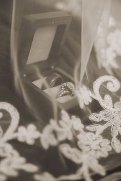 an open ring box sitting on top of a bed next to a lace covered sheet