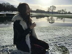 a woman sitting in the snow next to a lake