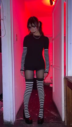 a woman in black and white striped stockings is standing in a hallway with red light