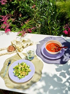 there is a bowl of soup next to a plate of salad on a table outside