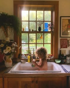 a young child sitting in a kitchen sink next to a window with flowers on it