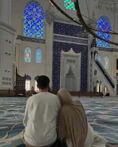 two people sitting on the ground in front of a building with blue and white stained glass windows