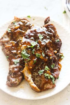 two pieces of meat covered in sauce and parsley on top of a white plate