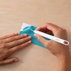 two hands holding a piece of blue paper and a white toothbrush on top of it