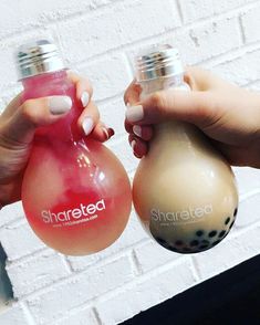 two women holding up small bottles in front of a white brick wall with the word shareea on it