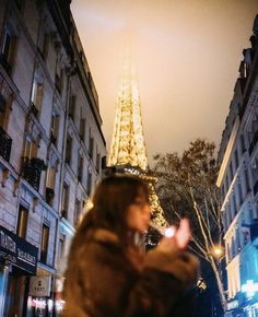 a woman standing in front of the eiffel tower on a city street at night