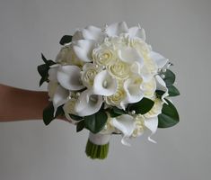 a bridal bouquet with white flowers and greenery is held by a woman's hand