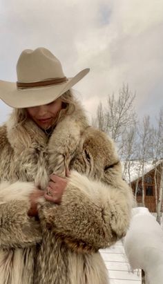 a woman wearing a fur coat and hat standing in the snow