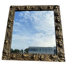 a mirror that is sitting in front of a building with blue sky and clouds behind it