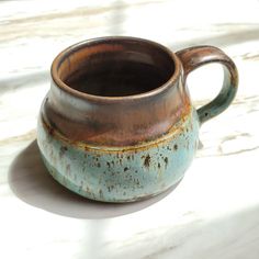 a brown and blue cup sitting on top of a white counter next to a window