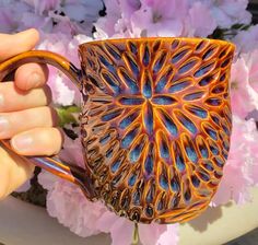 a person holding a coffee mug in front of some flowers