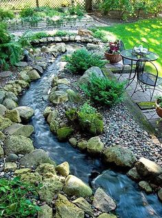 a small backyard with rocks and water running through the center, surrounded by greenery